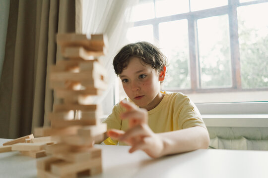 A father and son play a block tower game together indoors. The game is taking place on a white table, and the background is out of focus. Father's day