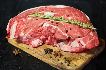 Pieces of raw meat lie on a wooden board surrounded by vegetables and spices. Meat production