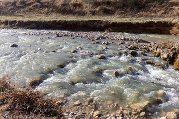 A shallow riverbed with an exposed rocky bottom, a small stream and a flow of water, autumn in nature