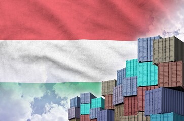 Hungary flag and big stack of shipping cargo containers in docks with sky background close up