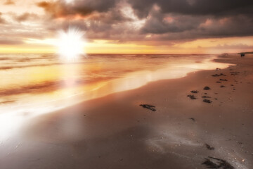 Sunset, beach and sea for vacation, holiday and travel to Denmark in summer. Ocean, lens flare and sand on coast with sky, nature or clouds on horizon with calm waves on landscape outdoor in Jutland