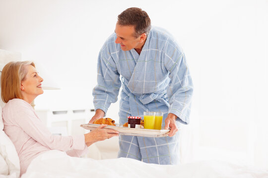 Couple, happy and serving breakfast in bed for nutrition, diet health and bonding together in home. Love smile, woman and man with food tray for morning meal, romantic support and eating in bedroom