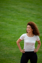 A beautiful curly girl posing in a white T-shirt and black leggings. Against the background of the stadium. Suitable for mockup