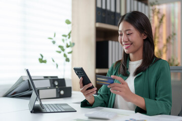Fototapeta premium Confident Asian businesswomen sitting at their desks Are using banking applications to buy or pay online mobile bills. and registered her credit card on the website for online purchases.