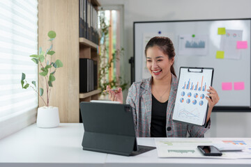 Asian businesswoman sitting in an office looking with graph detail on laptop computer Chart of real estate business growth data in the office.