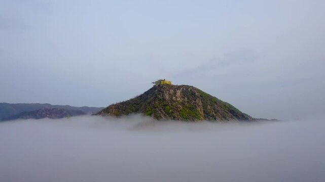 Aerial drone orbit shot Savitri Mata mother mandir temple perched at the peak of an Aravalli mountain emerging from clouds accessible only via ropeway or stairs a landmark and tourist spot