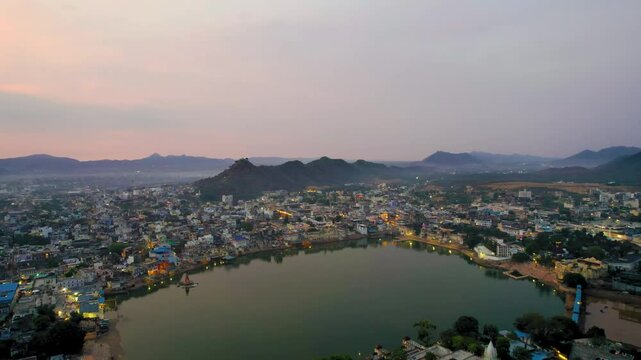 Night aerial drone shot flying towards pushkar lake cityscape showing buildings with lights and aravalli hills in the distance showing holy town in rajasthan India
