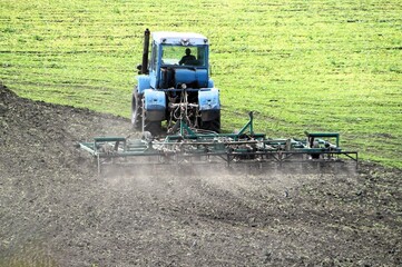 A blue tractor plows and sows a field in the spring, sowing.