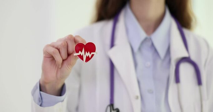 Woman doctor holds heart-shaped brooch adorned with heartbeat line graph. Touch of personality to cardiologist professional outfit in modern hospital