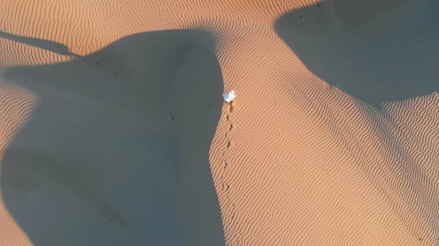 A man walking on a sand dune during sunrise as viewed from a drone. Liwa desert, United Arab Emirates.