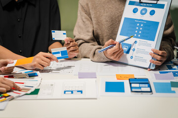 Close-up of hands working on UX/UI design at a desk. Papers with wireframes, prototypes, and...