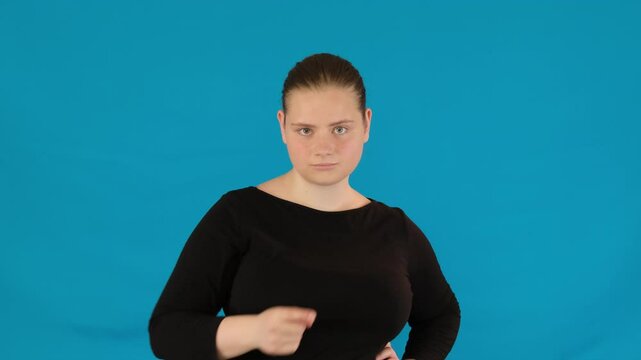 Woman waves finger with sense of reprimand on blue background. Lady tells off opponent by clear gesture with fierce glare in eyes