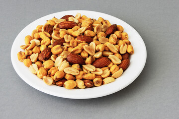 Roasted peanuts, corn and almonds on a plate on a gray background