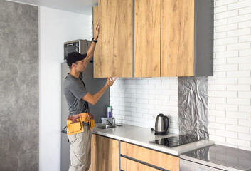 The carpenter finalizing the assembly of the kitchen shelf on the wall.