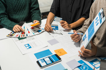 A group of people collaborates around a desk, discussing and reviewing user interface (UI) and user...