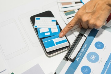 A group of people collaborates around a desk, discussing and reviewing user interface (UI) and user...