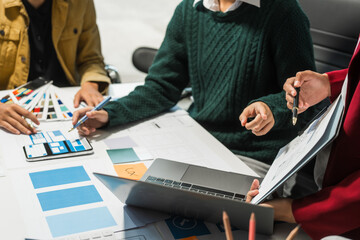 A group of people collaborates around a desk, discussing and reviewing user interface (UI) and user...