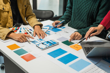A group of people collaborates around a desk, discussing and reviewing user interface (UI) and user...