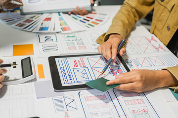 A group of people collaborates around a desk, discussing and reviewing user interface (UI) and user...