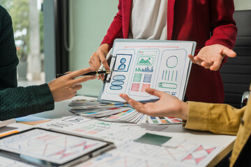 A group of people collaborates around a desk, discussing and reviewing user interface (UI) and user...
