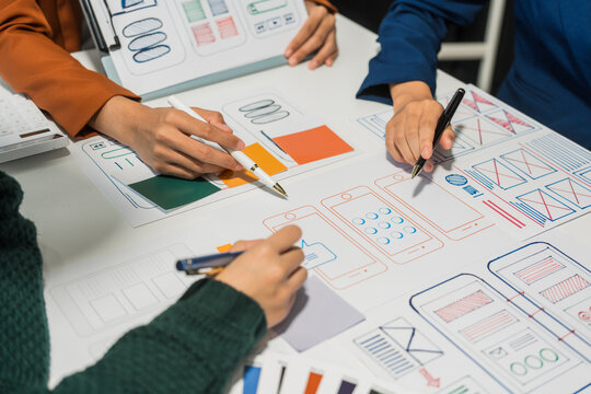 A group of people collaborates around a desk, discussing and reviewing user interface (UI) and user experience (UX) elements. usability, accessibility, and design principles for product development.