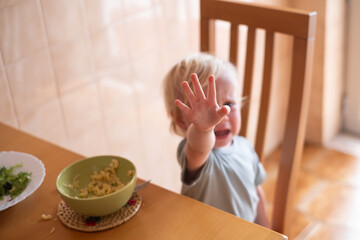 Beautiful blond child eating and crying with tantrum at home.