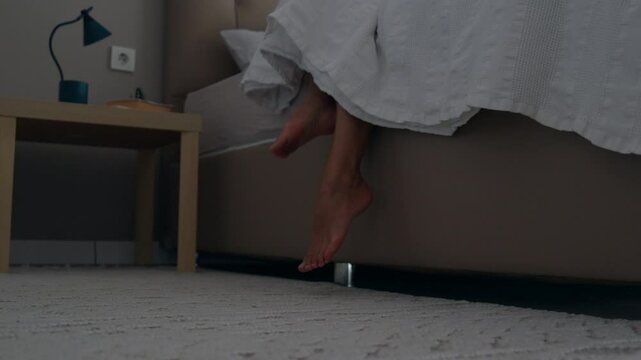 woman legs steps on the floor from bed