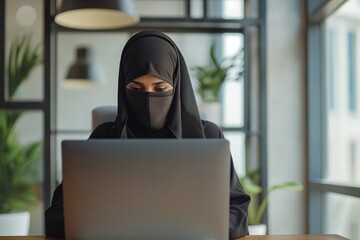 A successful programmer in niqab is typing on a laptop, involved in cyber activities with secure data.