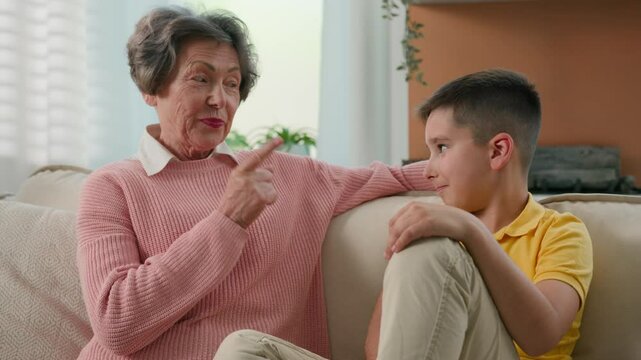 Caucasian grandmother explaining punishing spoiled grandson strict shaking index finger elderly caring woman grandma explain teaching discipline grandchild child kid boy on couch at home happy family