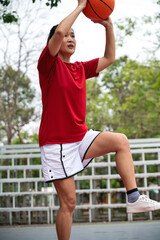 Vertical female basketball player shooting ball in outdoor court