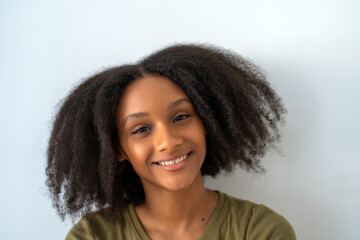 Portrait of smiling young African American woman with natural curly hair against plain background. 