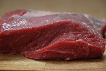 piece of cut red meat with visible fat on a wooden kitchen chopping board