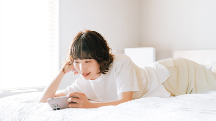 ベッドに寝転んでスマホを使う笑顔の日本人女性