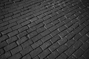 The texture of dark paving stones. Top view of the cobblestone pavement. An old stone sidewalk. The texture of the paving stones. The background is made of cobblestones, the road is made of cobbleston