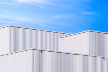 Fototapeta premium Group of 3 industrial factory buildings with geometric pattern of white aluminium corrugated metal wall against blue sky background, low angle and perspective side view