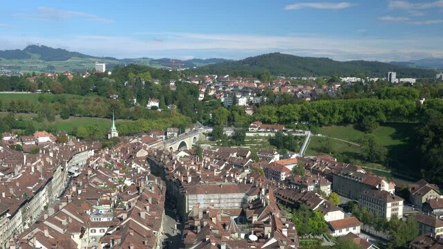 A cityscape with many buildings and a few trees. The sky is blue and the sun is shining
