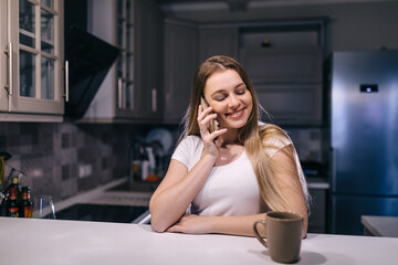 Cozy evening. Cheerful woman talking on the phone in the kitchen, free time