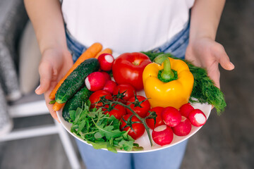 beautiful female hands holding a plate of fresh vegetables