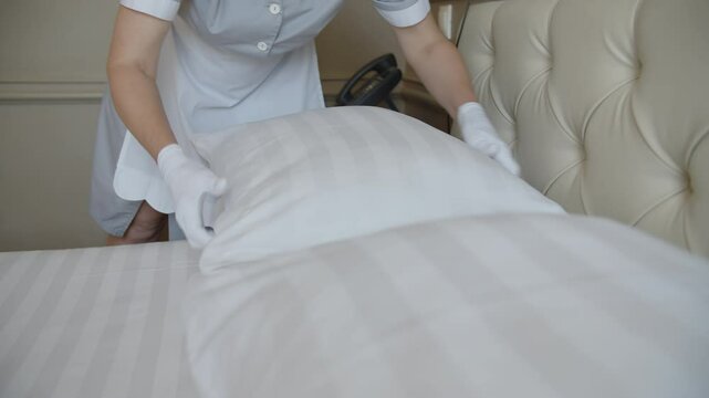 maid in gloves changing bed linen in hotel room, room service