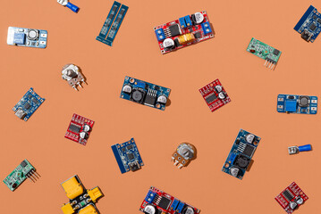Microcontrollers, boards, sensors, leds and modules for learning the basics of electronics. Various electronic components for soldering arranged in creative arrangement on orange background
