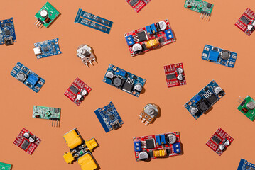 Microcontrollers, boards, sensors, leds and modules for learning the basics of electronics. Various electronic components for soldering arranged in creative arrangement on orange background