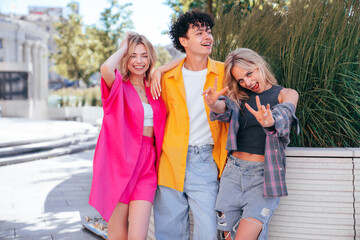 Group of young three stylish friends posing in the street. Fashion man and two cute female dressed in casual summer clothes. Smiling models having fun. Cheerful women and guy outdoors