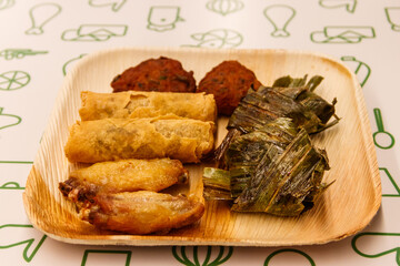 Set of thai food (fried chicken wrapped in pandan leaves, chicken wings, vegetable spring rolls, thai shrimp cake) on a table