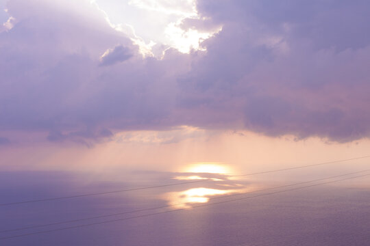Cloudy purple sky with sun rays falling into the sea