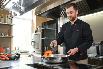 chef standing in restaurant and making flambe on frying pan