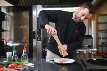 Chef in hotel or restaurant kitchen cooking, he is cutting meat or steak