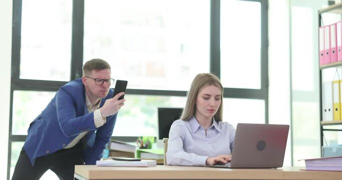 Focused businesswoman works on laptop while spying colleague takes picture of screen in office. Man steals data of business company