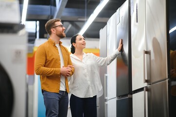 family couple buying domestic refrigerator in supermarket