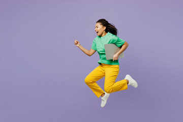 Obraz premium Full body young IT woman of African American ethnicity with dreadlocks wear t-shirt casual clothes jump high holding closed laptop pc computer isolated on plain purple background. Lifestyle concept.