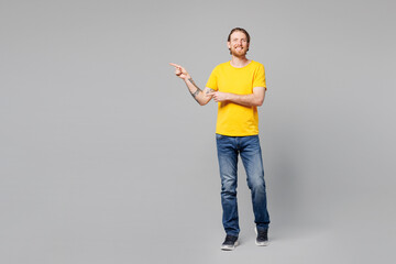 Full body young man he wear yellow t-shirt casual clothes point index finger aside indicate on workspace area copy space mock up isolated on plain grey background studio portrait. Lifestyle concept.